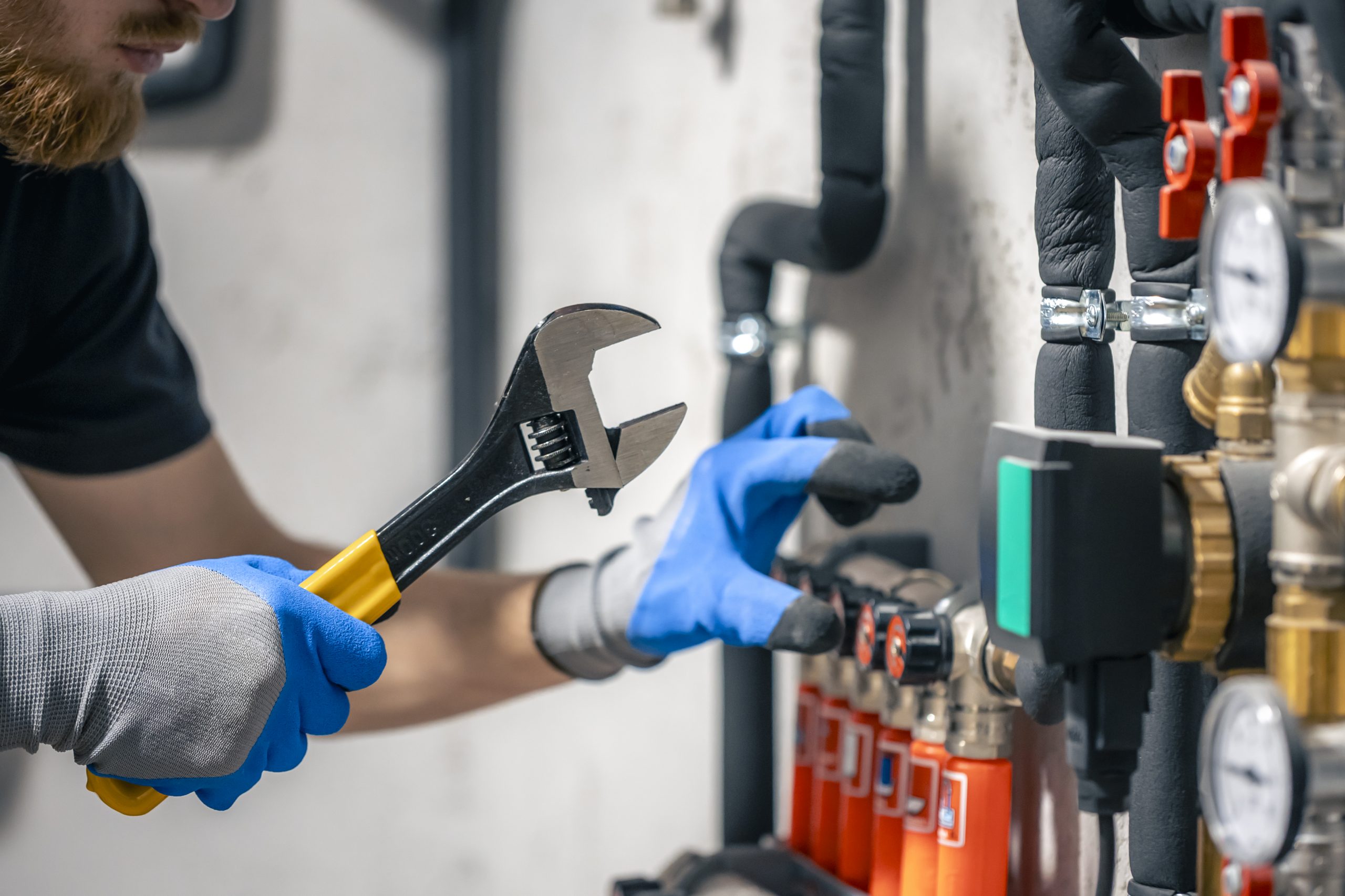A man installs a heating system in a house and checks the pipes with a wrench.